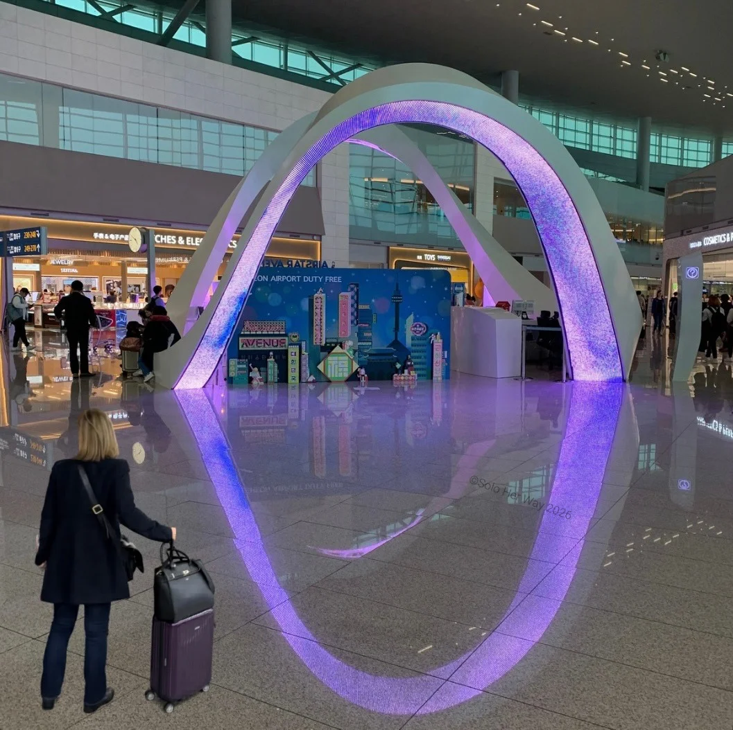 Purple glowing arch installation inside a modern airport with reflection on shiny floor and traveler with luggage