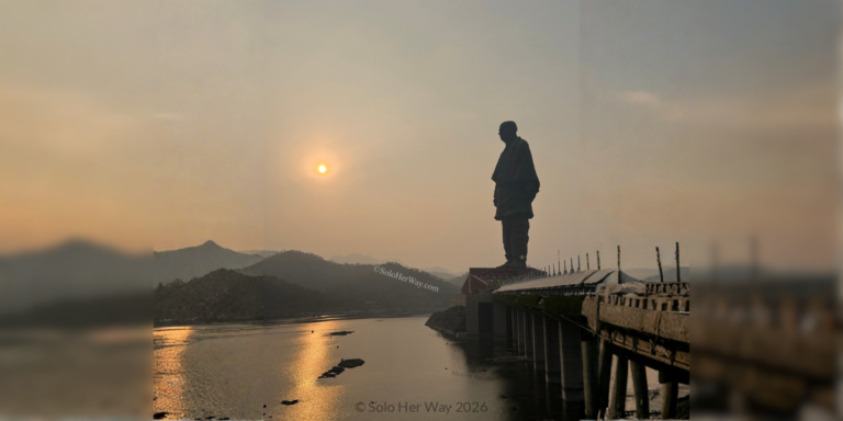 Statue of Unity at sunset beside the river with golden light, hills, and bridge leading toward the monument.