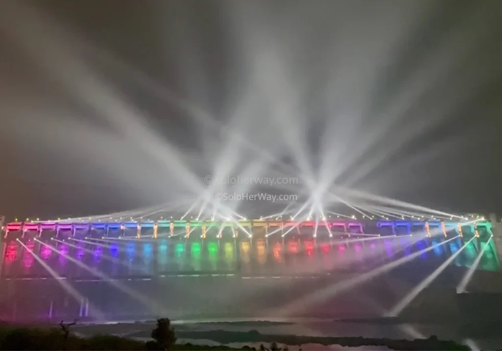 Visitors watching a vibrant nighttime light and laser show near the Statue of Unity with colorful reflections across the water.