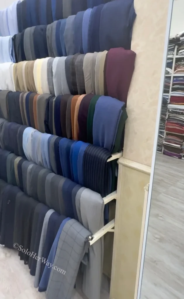 Getting Clothes Made in Hoi An & Ho Chi Minh City: What I Wish I’d Known 5 Rows of fabric samples displayed inside a tailoring shop, featuring various colors, textures, and materials used for custom-made clothing.