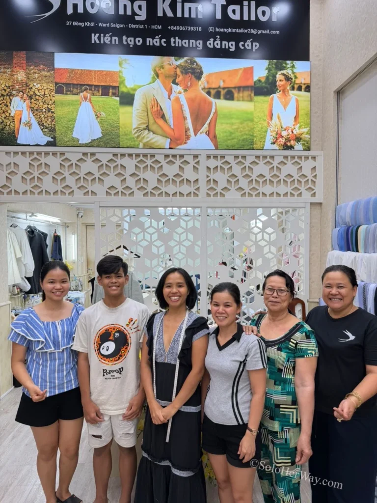 Getting Clothes Made in Hoi An & Ho Chi Minh City: What I Wish I’d Known 8 Tailoring team posing together inside a custom clothing workshop, representing the craftsmanship and expertise behind bespoke garments in Vietnam.