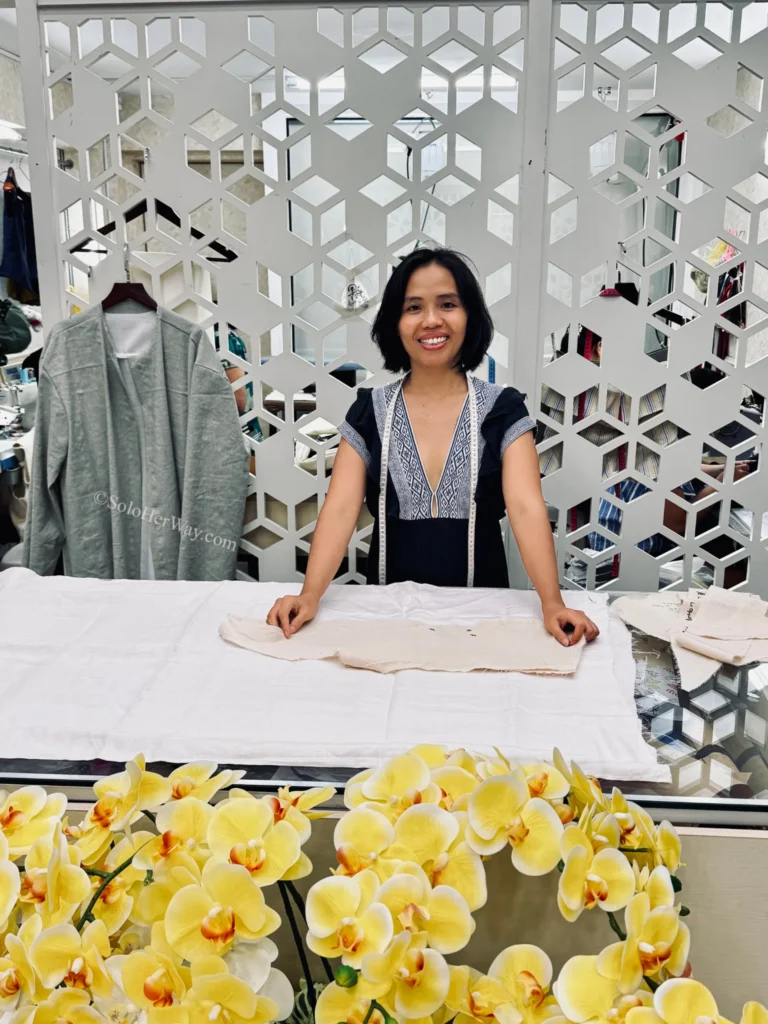 Getting Clothes Made in Hoi An & Ho Chi Minh City: What I Wish I’d Known 2 Professional tailor standing behind a worktable with fabric patterns, showcasing the skilled craftsmanship involved in custom clothing creation.
