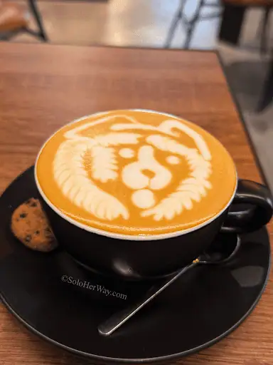Ho Chi Minh City cafe latte with lion art, served on a black saucer with a cookie, showcasing Vietnam’s vibrant coffee culture