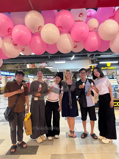 Ho Chi Minh City locals and travelers pose under pink balloons inside a lively shopping mall, capturing friendly city culture