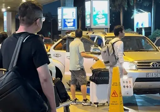 Ho Chi Minh City airport taxi pickup with travelers, luggage, and local cabs, showing transport and arrival in Vietnam.