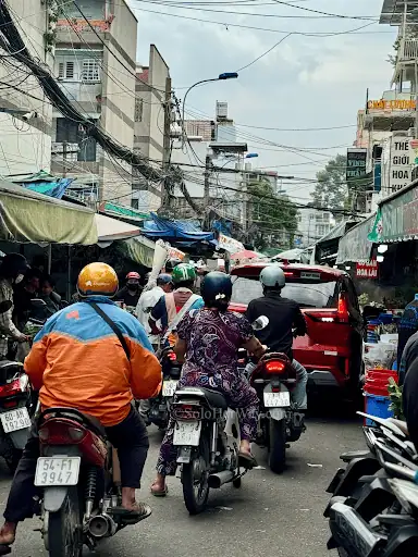 Ho Chi Minh City street scene with motorbikes, market stalls, local shops, and busy daily life in a vibrant Vietnam neighborhood.